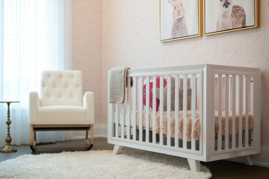 Chambre de bébé aux tons rose pâle avec lit à barreaux blanc, fauteuil à bascule et tapis moelleux